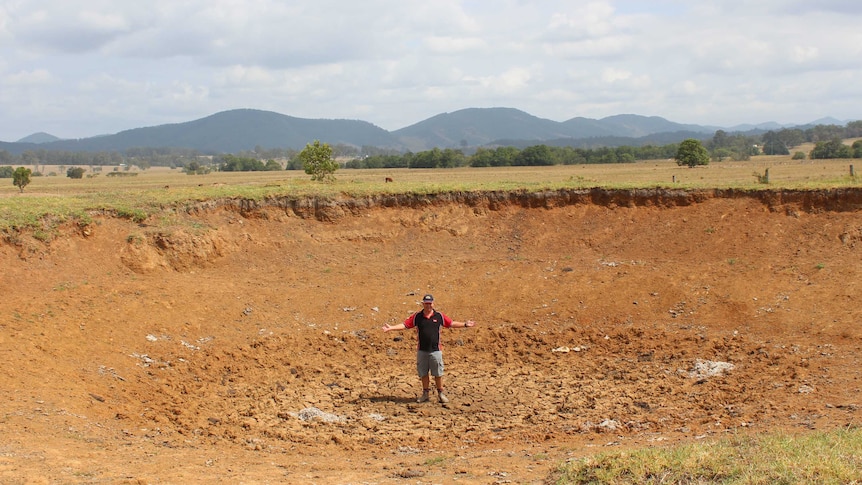 A man stands in the middle of a dry dam, surrounded by brown farmland.