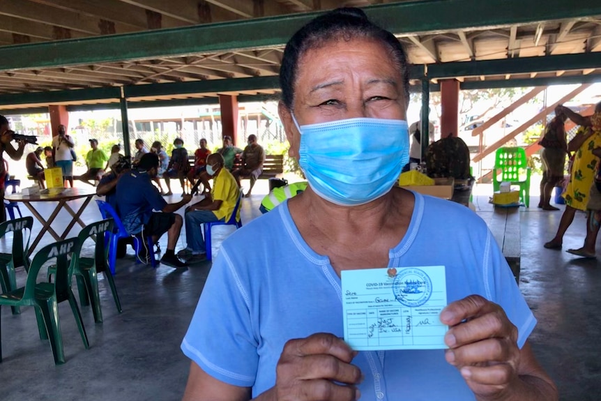 A woman wearing a surgical mask holds up a certificate.