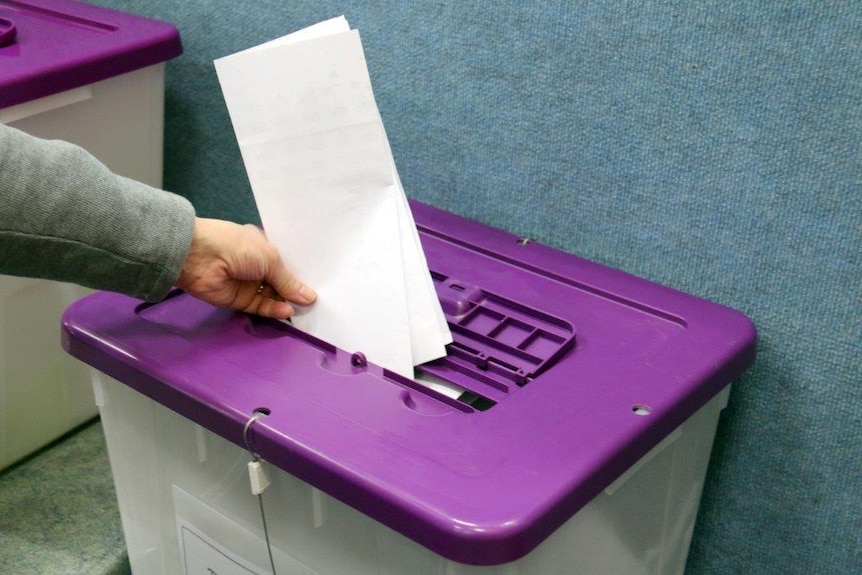 A voter puts a Senate paper into a ballot box for the 2016 federal election.