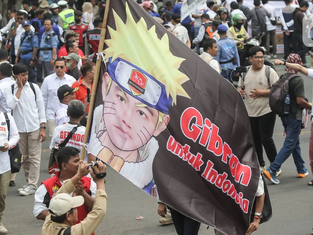 A man holding a banner on a stick with picture of Japanese character and said Gibran for Indonesia