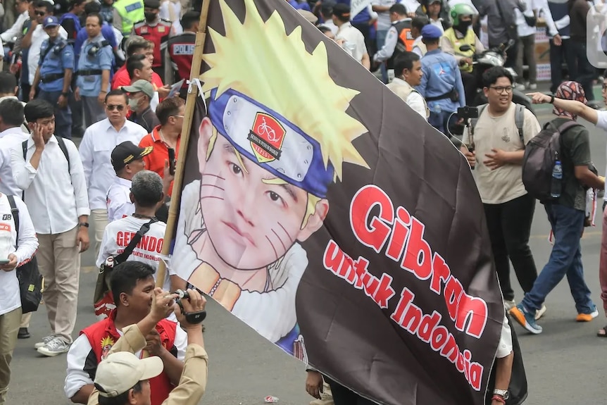 A man holding a banner on a stick with picture of Japanese character and said Gibran for Indonesia