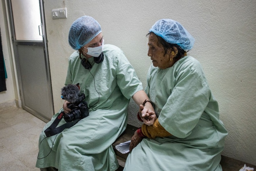 Woman in surgical scrubs holding camera and hand of woman in scrubs preparing for surgery.