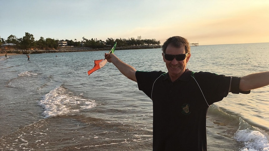 Tony Mangan stands beside the beach and holds an Irish flag