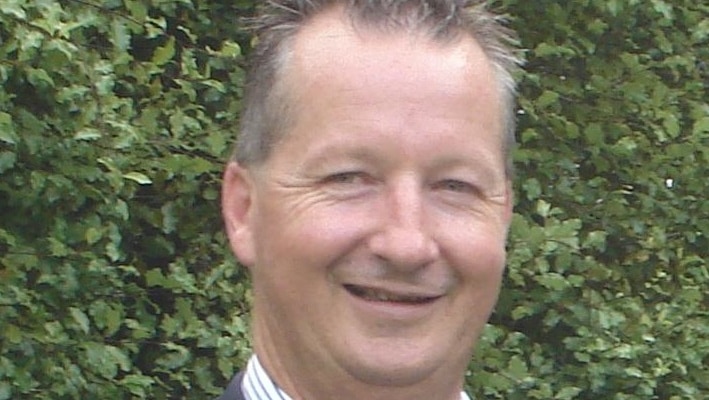 Peter Keeley, wearing a business shirt and jacket, poses for a formal photo.