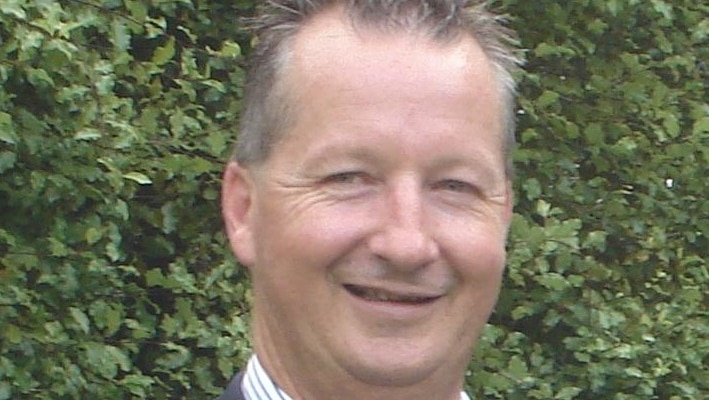 An older man wearing a business shirt and jacket, poses for a formal photo.