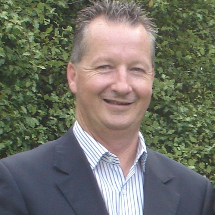 Peter Keeley, wearing a business shirt and jacket, poses for a formal photo.