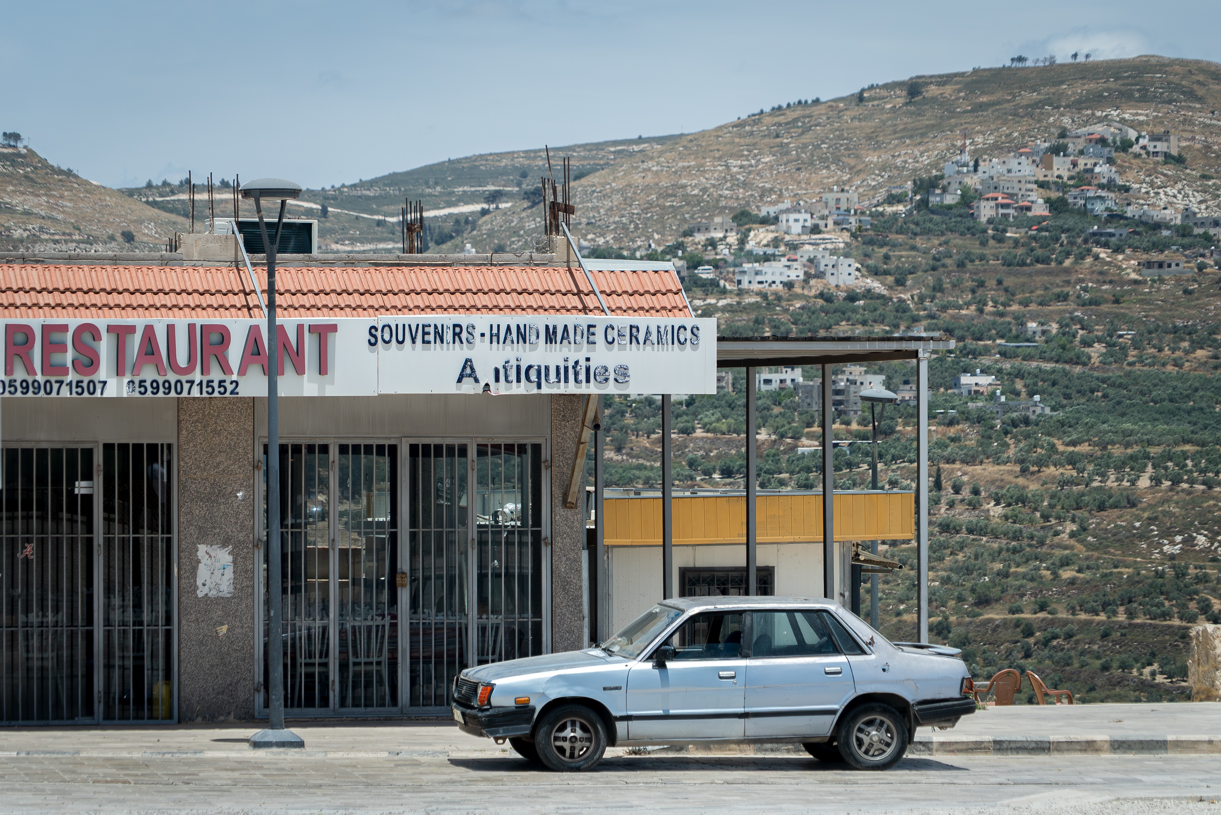 A close up of a storefront that is closed, with an old car parked out front.