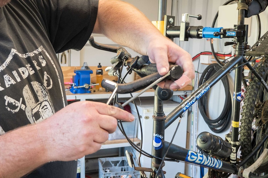 A man works to take apart the handlebars of a bike.