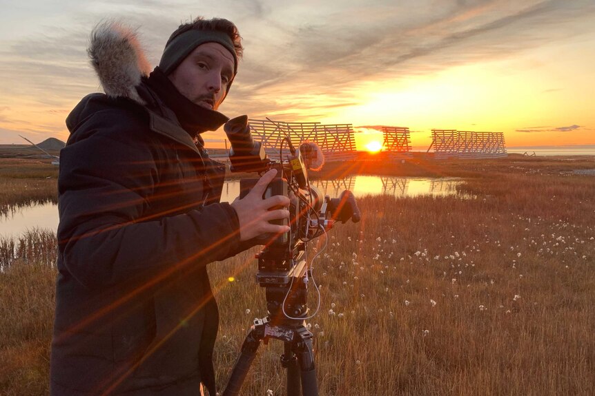 Cameraman filming sunset over Alaskan landscape.