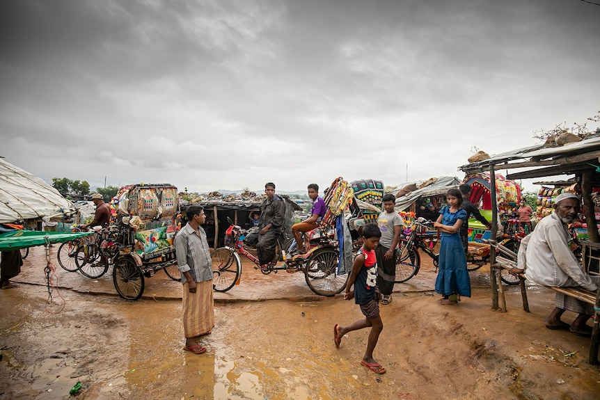 Men and women standing outdoors and on cycle rickshaws under an overcast sky.