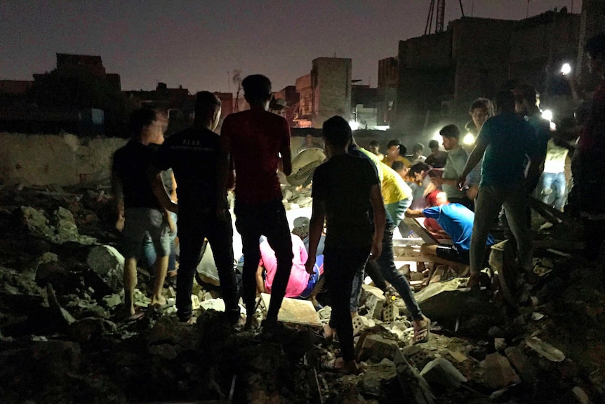A group of people are seen looking through rubble using flash lights at night.