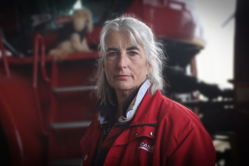 A grey-haired woman stands in a tractor shed.