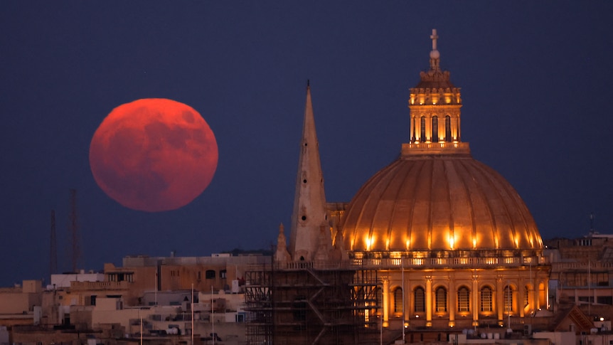 A large, full red moon behind a cathedral 