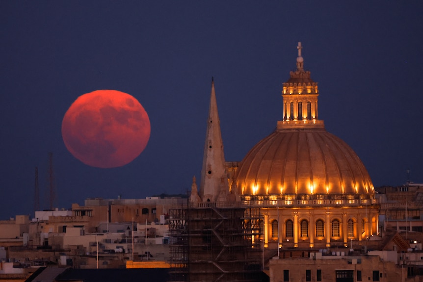 A large, full red moon behind a cathedral 