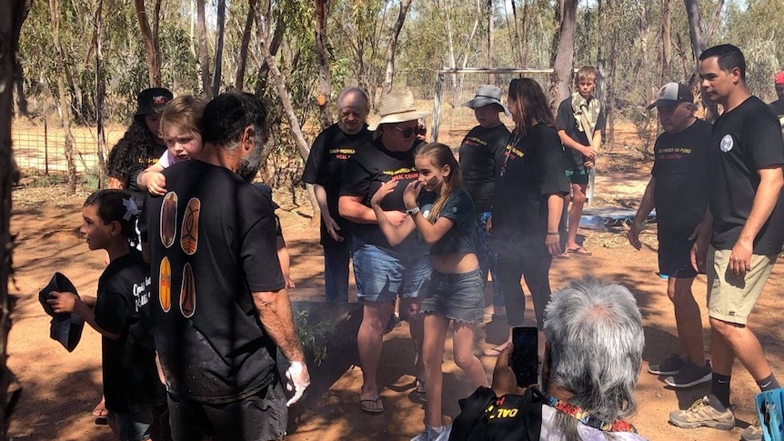 A crowd gathers round a fire pit for a traditional Indigenous smoking ceremony.