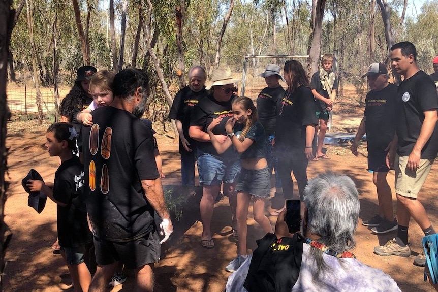 A crowd gathers round a fire pit for a traditional Indigenous smoking ceremony