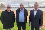 Three men stand facing the camera, against a backdrop of Port Pirie's lead smelter.