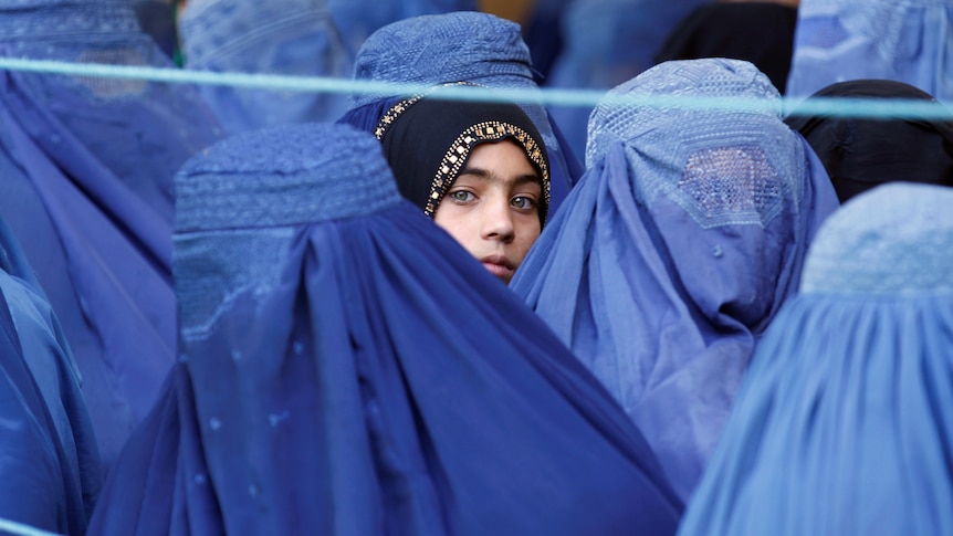 A girl looks on among Afghan women completely covered by blue burqas.