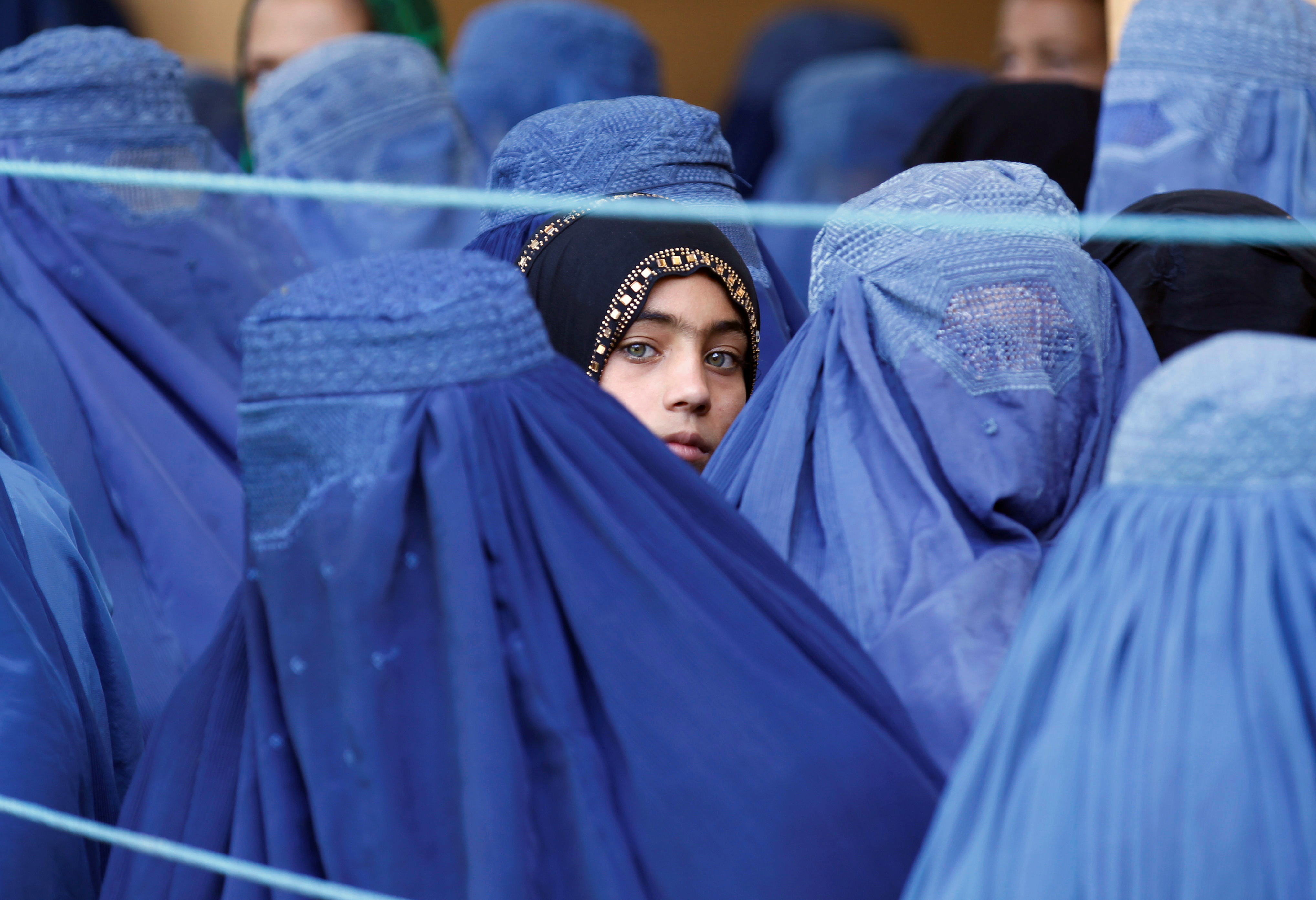 一个女孩在阿富汗妇女中间看着男人完全被蓝色罩袍所覆盖。” class=