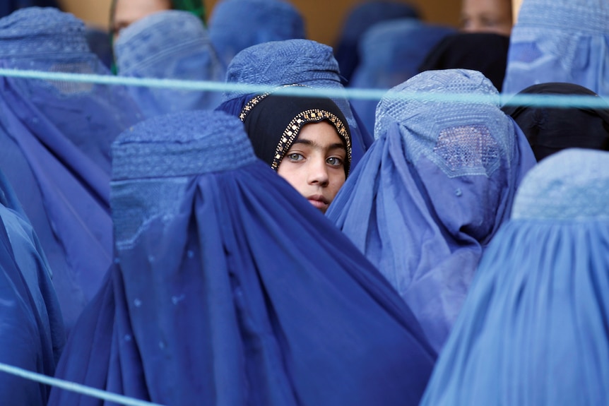 A girl looks on among Afghan women completely covered by blue burqas.