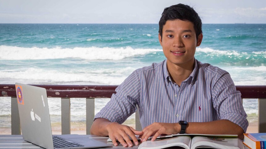 Medical student Dominic Ku sits at a table with books and a laptop.