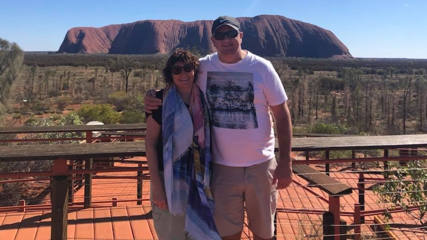 A man and woman standing side-by-side in front of Uluru