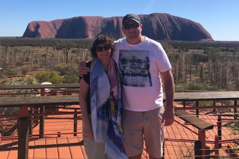 A man and woman standing side-by-side in front of Uluru