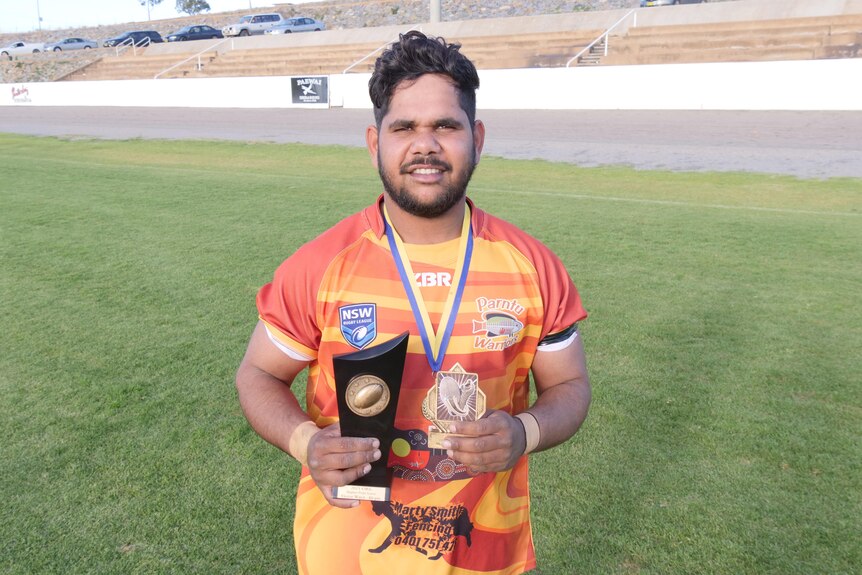 Victor Ward wears his grand final medal and holds two awards.