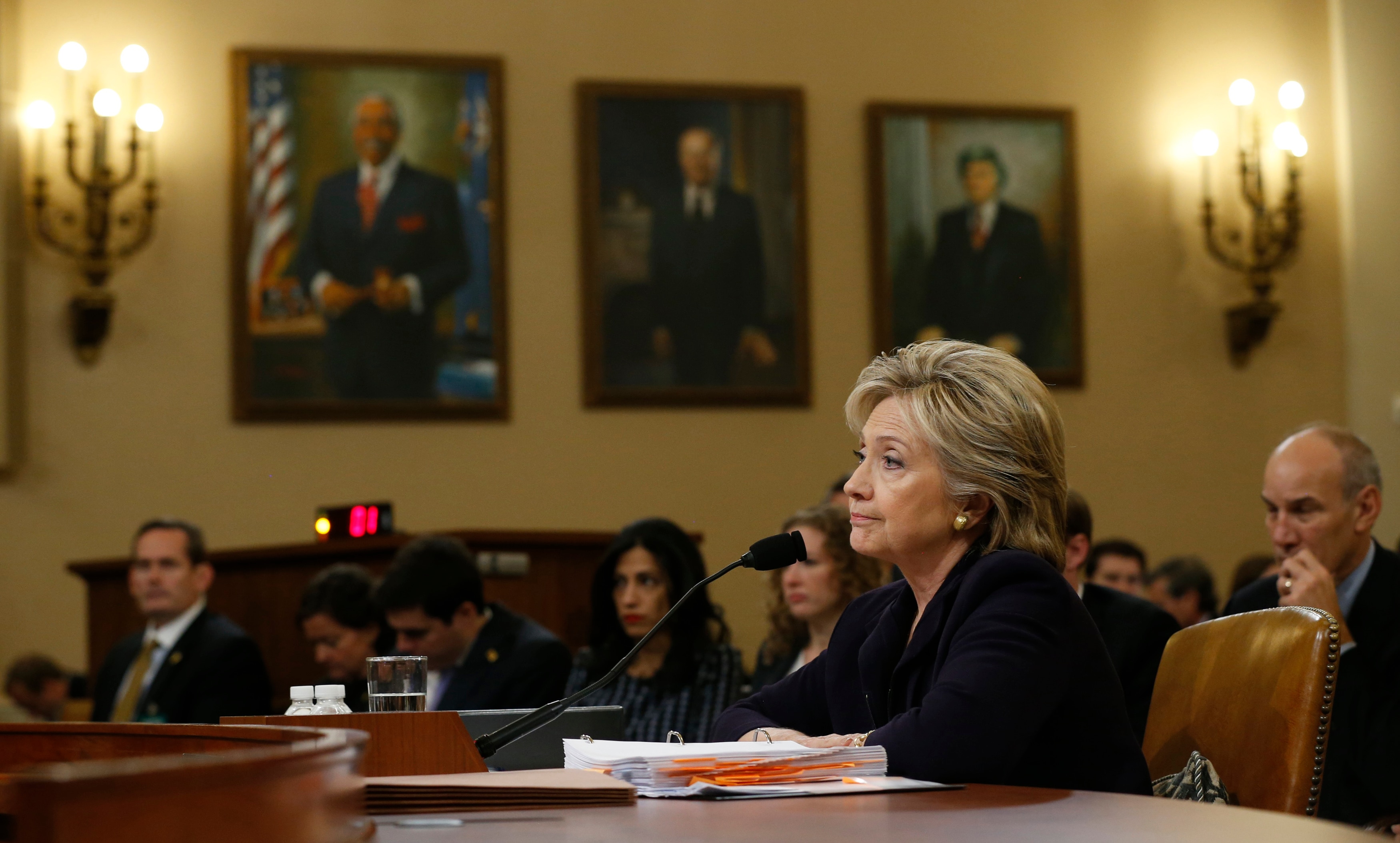 Hillary Clinton, harta, se sienta en una sala de audiencias del Congreso de Estados Unidos, escuchando una pregunta, frente a un montón de papeles.