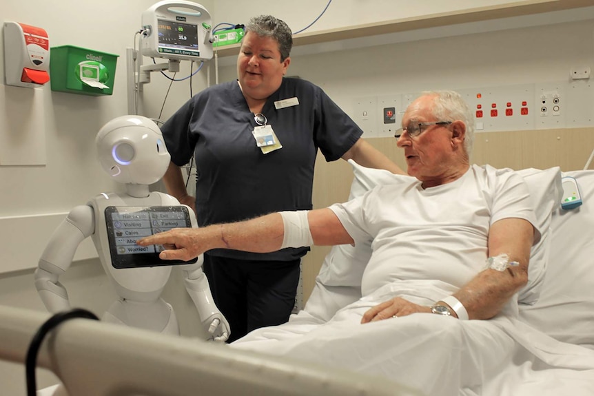A humanoid robot and a nurse stand at the bedside of a patient at the Townsville Hospital.