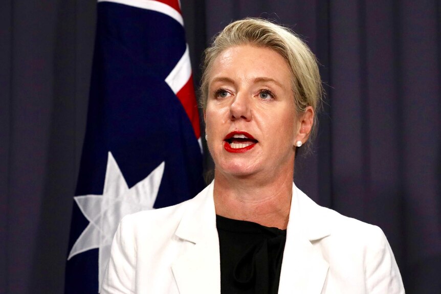 Senator McKenzie is mid sentence, wearing a white blazer and has her hair pulled back.