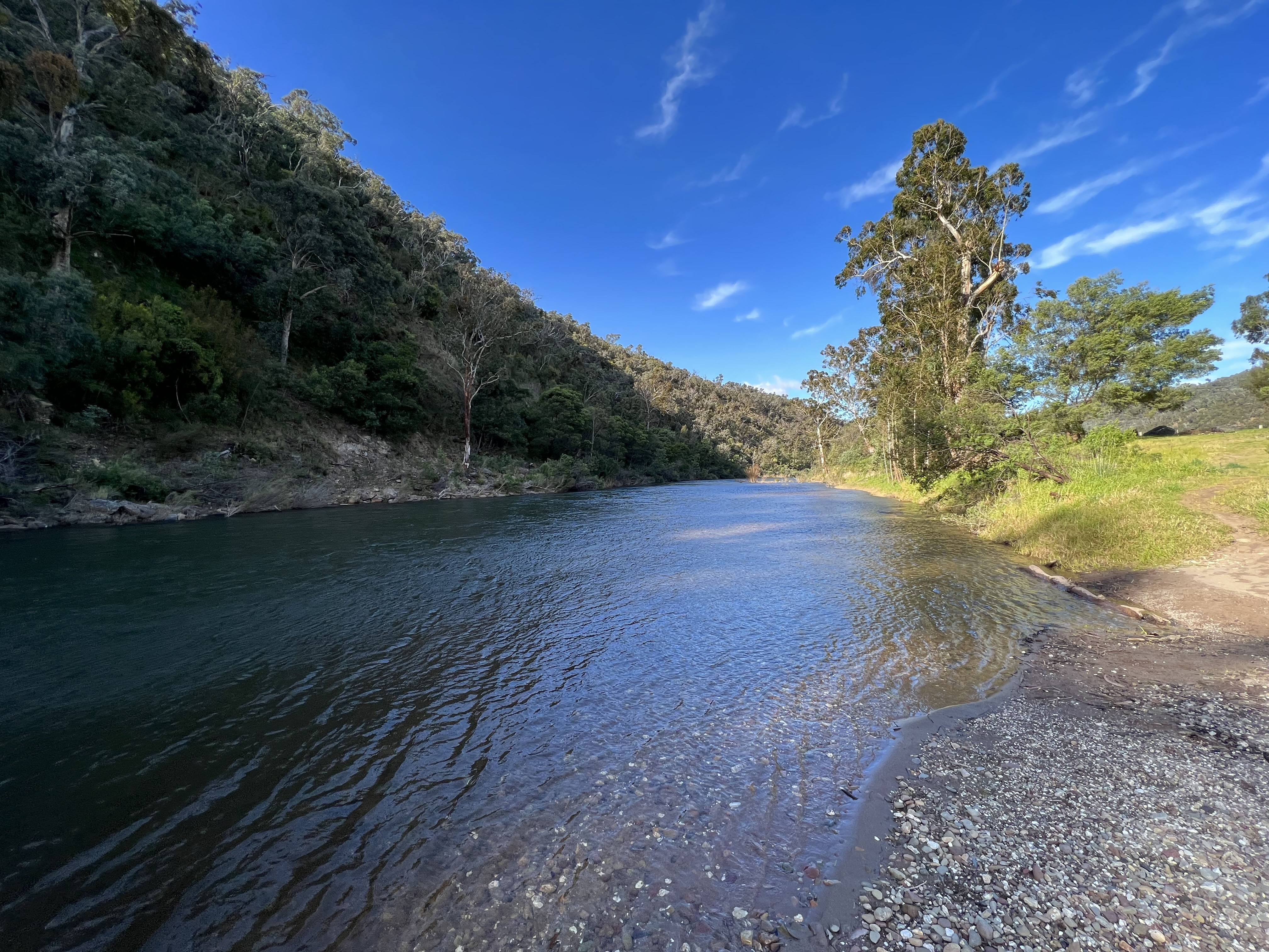 The wide Macalister River flows between a rocky hill and green campsite.