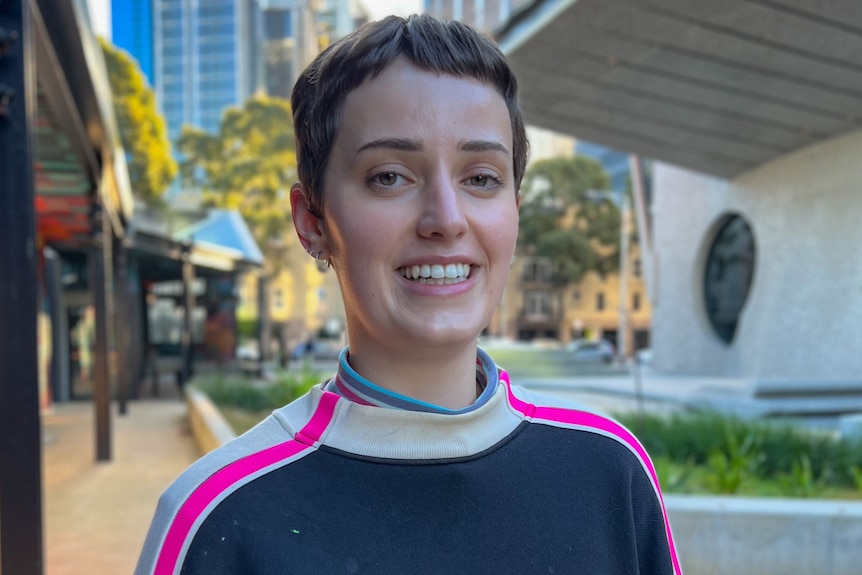 A woman is smiling at the camera. She has short brown hair and is wearing a colourful jumper.