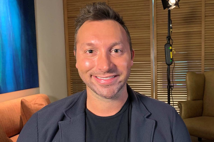 Ian Thorpe smiles at the camera. Behind him, studio lights are visible