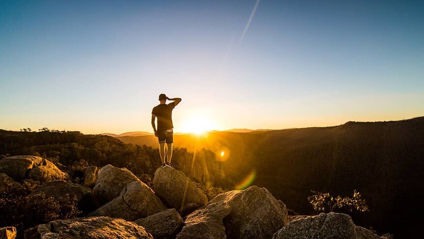 A person stands on a rocky outcrop at sunset.