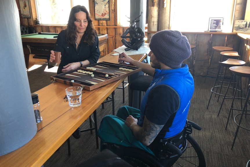 Sam Tait sits in his wheelchair holding a dice roller opposite his mother as both look over a backgammon board.