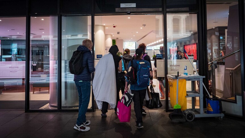 A group of people enter the Mercure hotel in Sydney carrying bags.