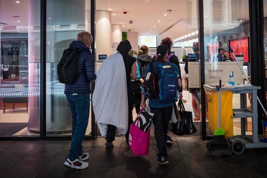 A group of people enter the Mercure hotel in Sydney carrying bags.