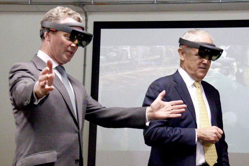 Christopher Pyne spreads his hands in front of him, while wearing mixed reality hollow lenses with Malcolm Turnbull.