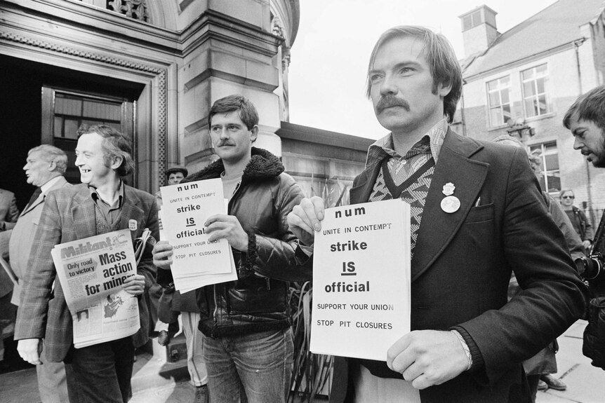 Striking miners in 1980s England hold newsletters and posters.