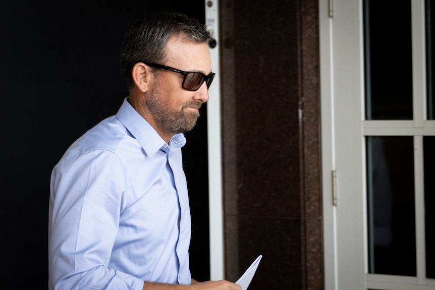 A man in a blue long-sleeved shirt and sunglasses walks out of the doors of the NT Supreme Court.