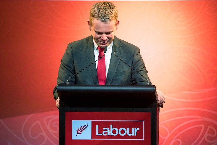Chris Hipkins bows his head while standing at the lectern. 