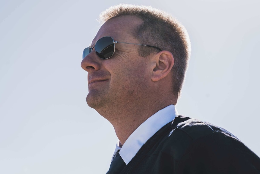 A pilot wearing sunglasses against a grey sky.