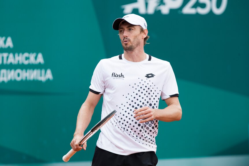 John Millman blows air out of his mouth through pursed lips and looks off to his right