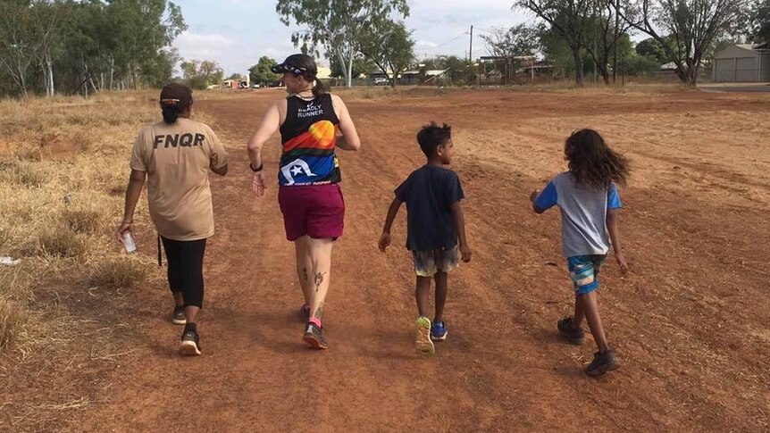 Two adults and two children walk and run in Doomadgee