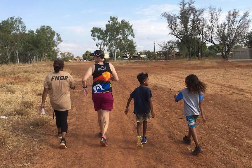 Two adults and two children walk and run in Doomadgee