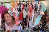 Two women poking their heads through a clothes rack