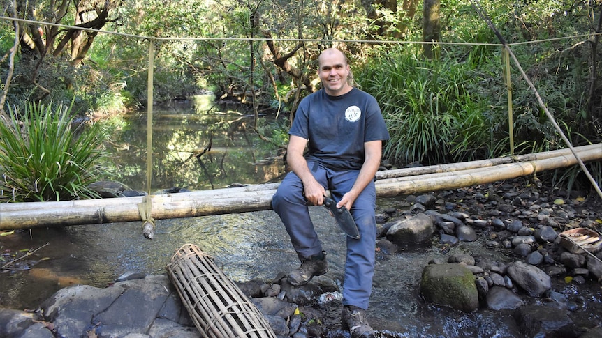Scott Poad sitting on hand-made bamboo log bridge across a small stream in the bush.