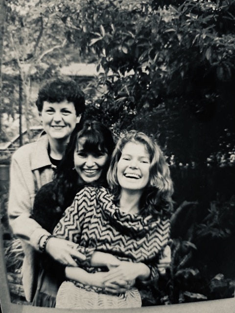 Altes Schwarz-Weiß-Foto von Patti in ihren Zwanzigern mit zwei Freundinnen in einer großen Umarmung.