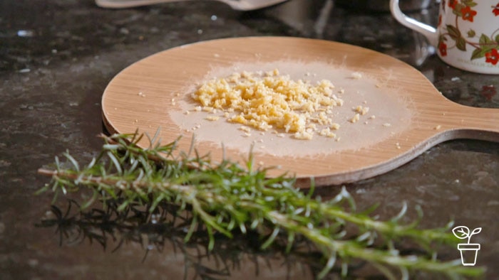 Circular wooden board with grated lemon and rosemary in foreground